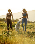 Two women walking a dog in a field and held pouch go Rigby Dog treat with mountains in the background