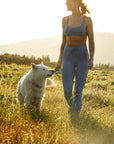 Woman in athletic wear feeding Rigby Dog Treat Pouch to a white dog in a field with mountains in the background