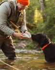 Man in outdoor gear interacting with a black dog in a forest setting