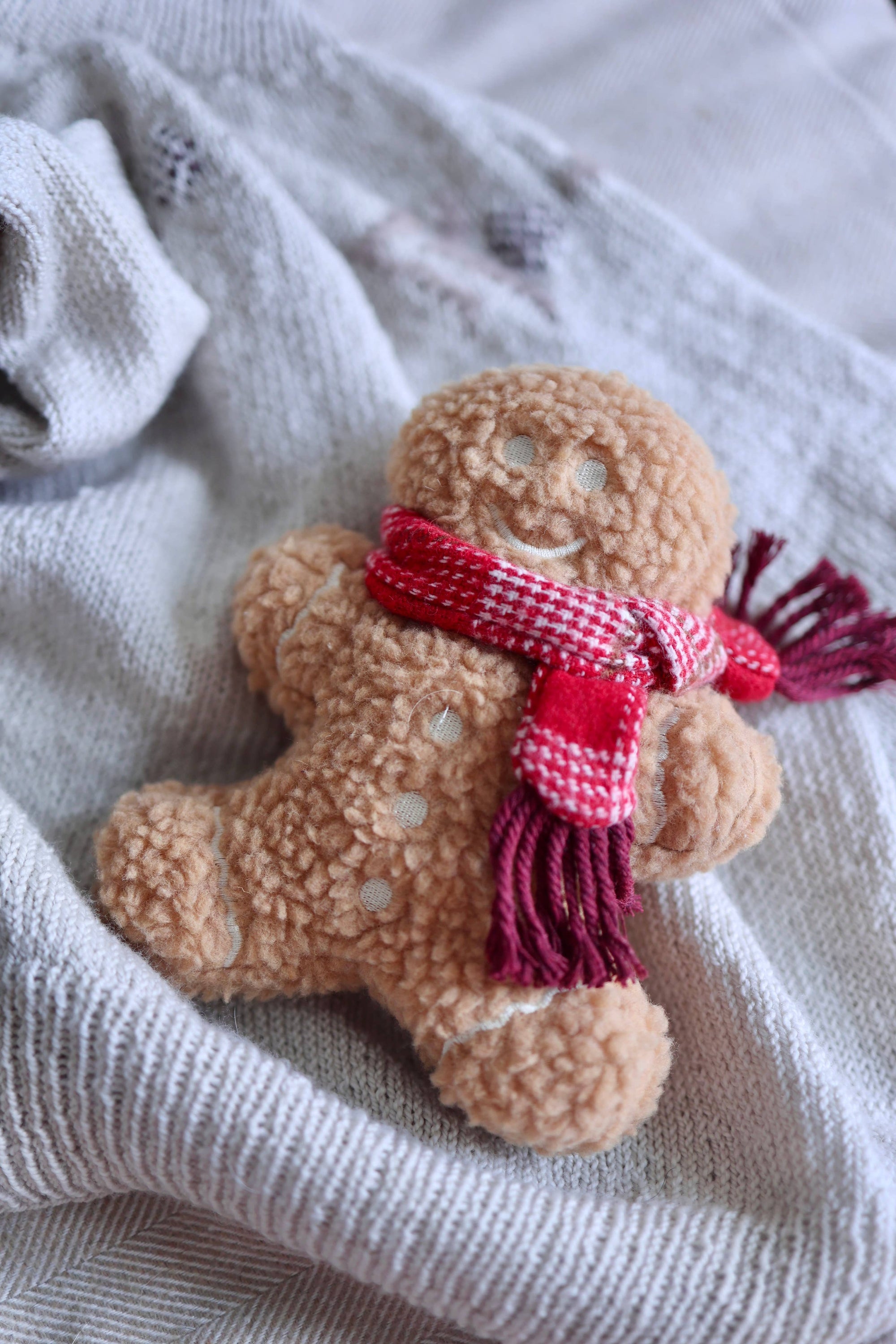Gingerbread man toy with a red scarf on a textured fabric background