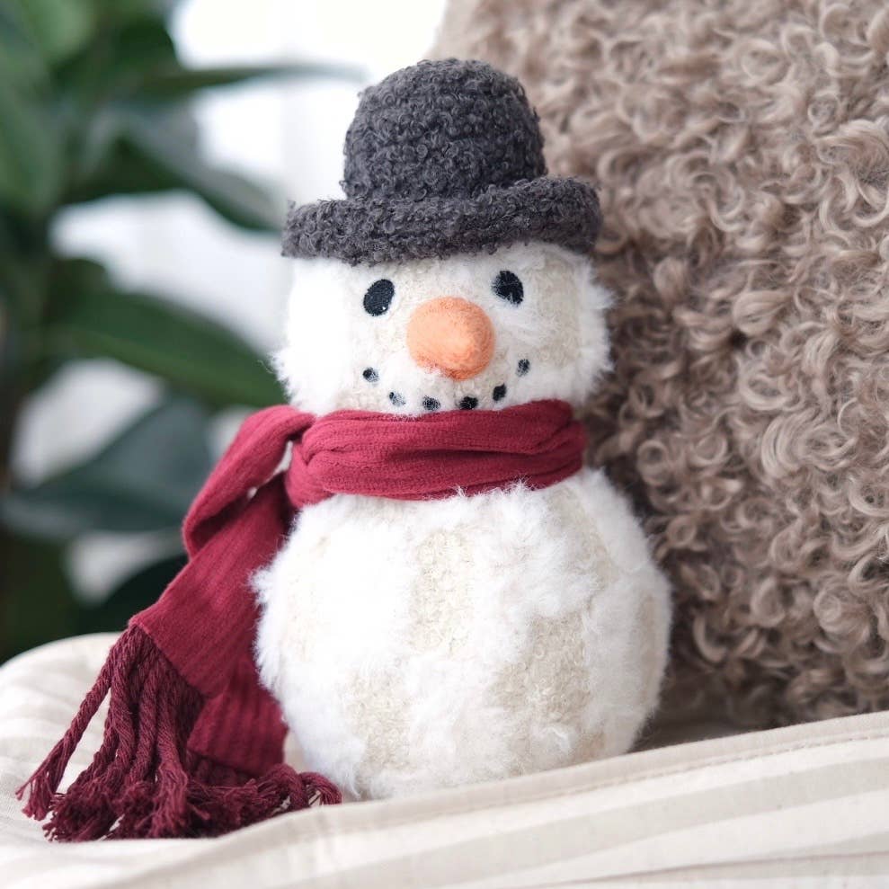 Small snowman dog toy with a red scarf and gray hat on a white surface.