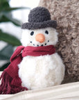 Small snowman dog toy with a red scarf and gray hat on a white surface.
