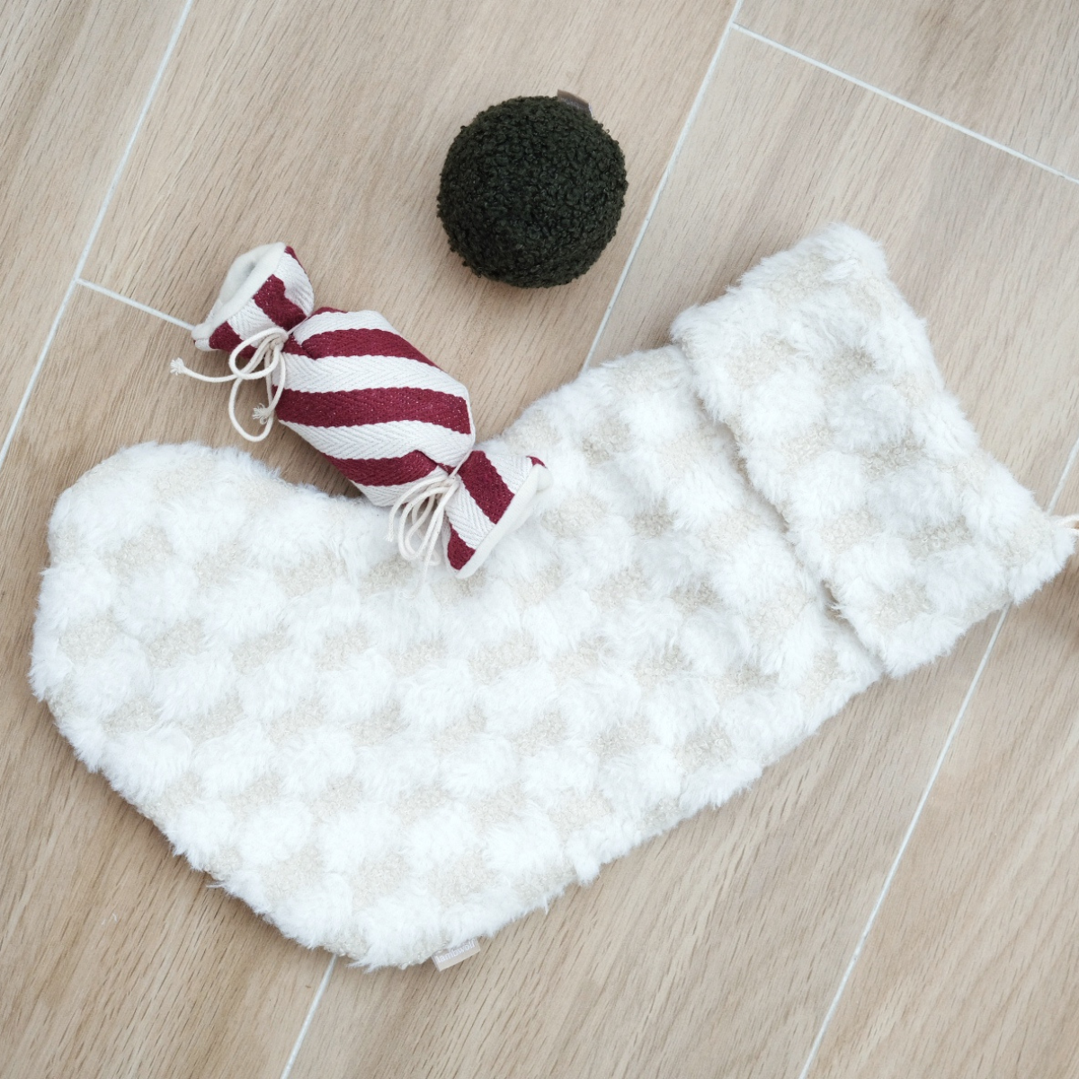 White fluffy dog coat with a red and white striped candy toy and black ball on a wooden floor.