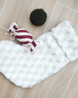 White fluffy dog coat with a red and white striped candy toy and black ball on a wooden floor.